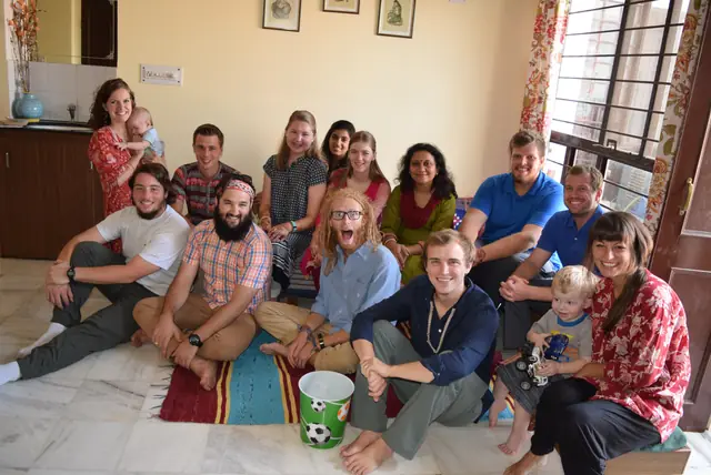 A large group of guests and hosts sitting together on the floor of a family home