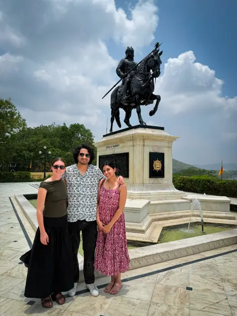 Three people in front of a bronze equestrian memorial on a hillside
