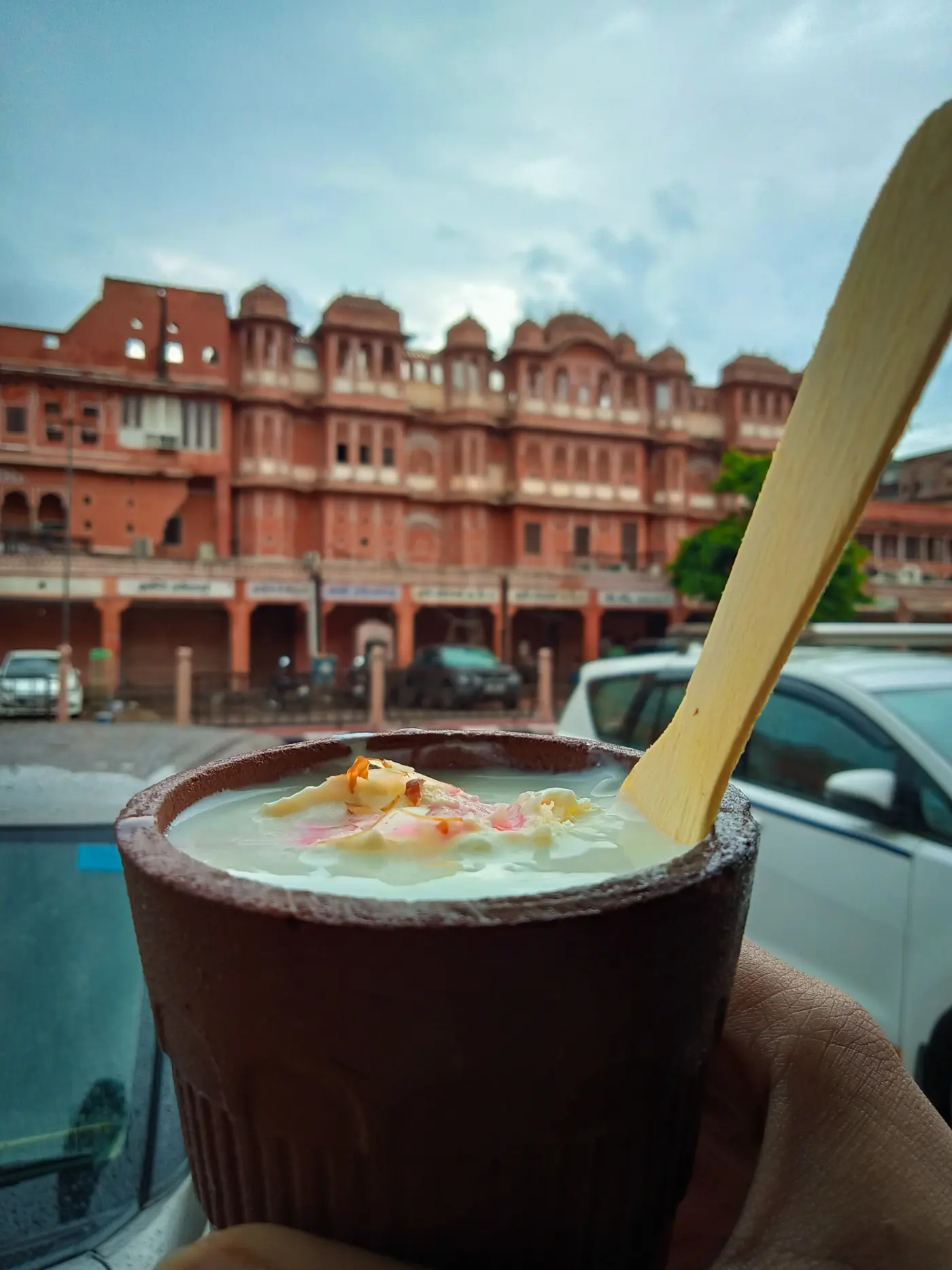 A clay cup of lassi held up in front of Hawa Mahal in Jaipur
