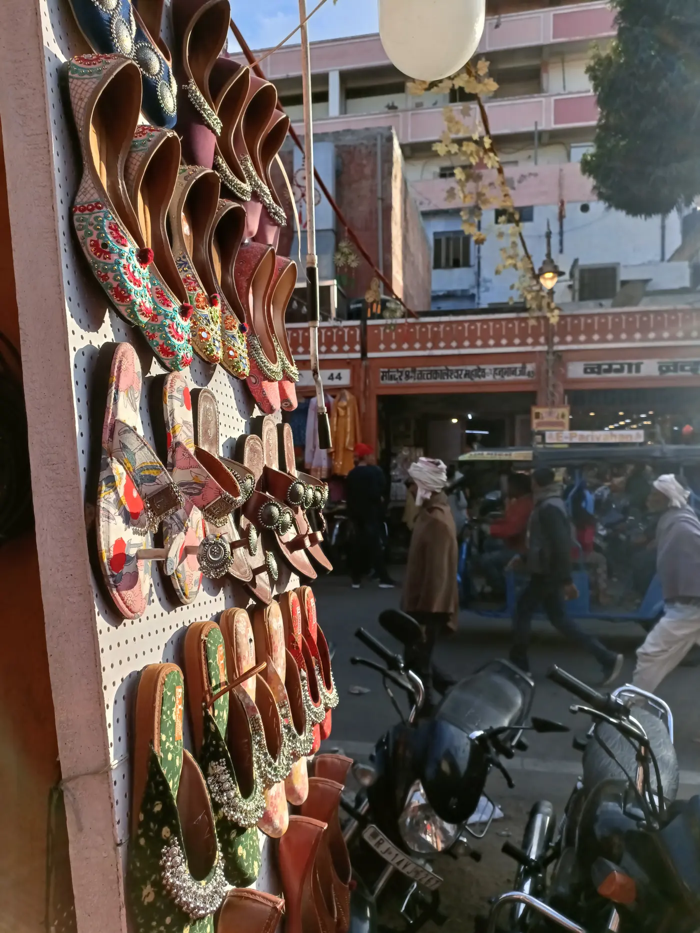 Embroidered leather juttis on a shop board, the bazaar street beyond