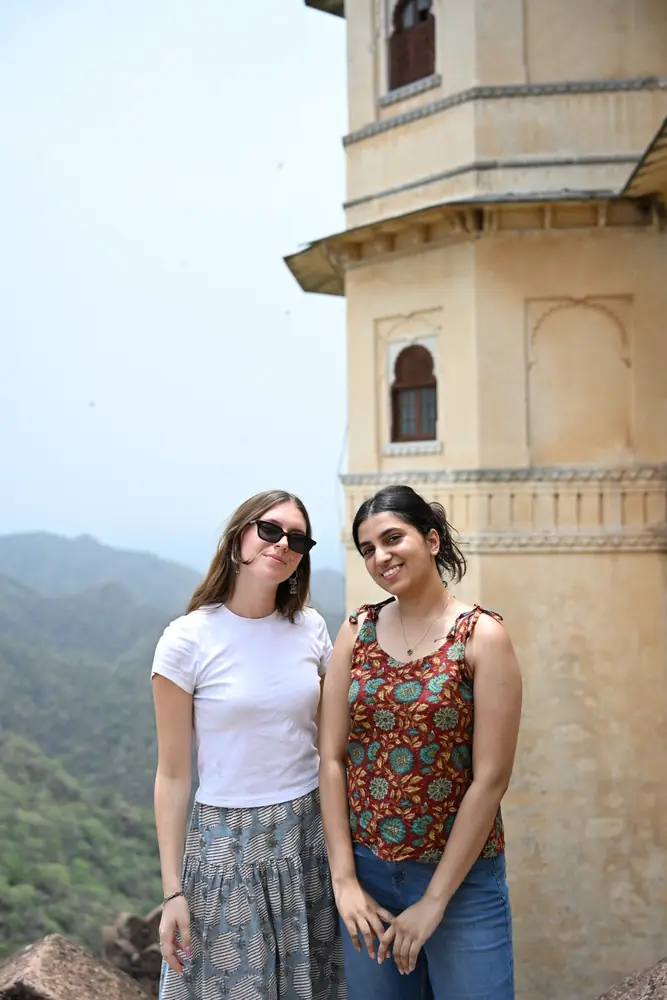Two travellers at a hilltop palace with green hills behind them
