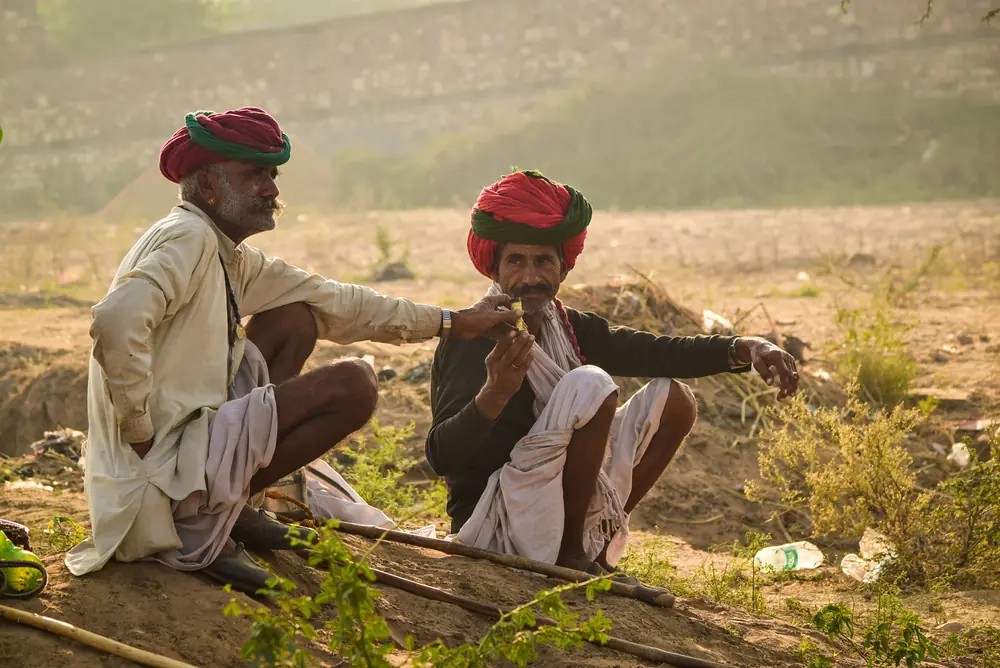 Two men in red turbans sitting together at the edge of a field