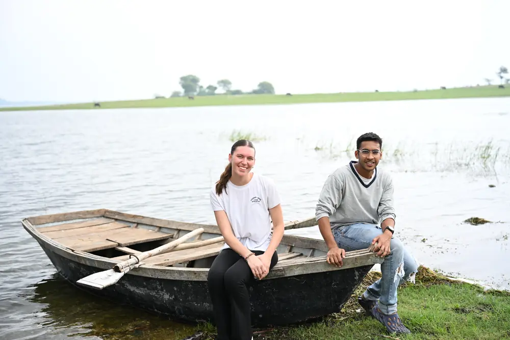 Two travellers sitting on a wooden boat at the edge of a flooded lake