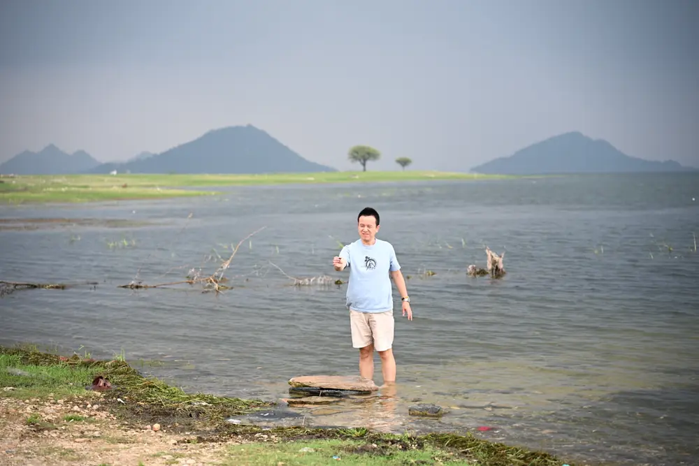 A traveller standing in the shallows at a lake edge, hills beyond
