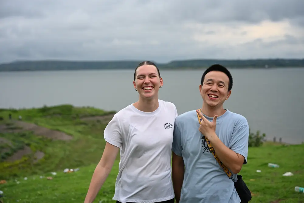 Two travellers laughing on the green bank above the water